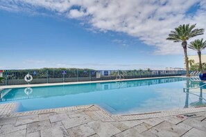 A clear blue swimming pool with a lifebuoy, a fence, and palm trees. - Sterling Breeze 507- Dancing Waves (Panama City Beach)