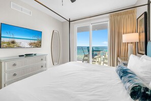 A hotel room with a large bed, a flat-screen TV, a dresser, and a balcony with a view of the ocean. - Sterling Breeze 507- Dancing Waves (Panama City Beach)