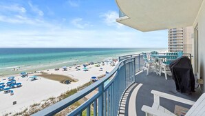 Ein Balkon mit Blick auf Strand und Meer, Sitzgelegenheiten im Freien und ein Grill.
