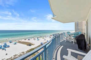 A balcony with a view of a beach and ocean, outdoor seating, and a grill. - Sterling Breeze 507- Dancing Waves (Panama City Beach)