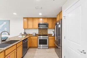 A modern kitchen with wooden cabinets, stainless steel appliances, granite countertops, and a stainless steel sink. - Sterling Breeze 507- Dancing Waves (Panama City Beach)