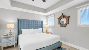 Ein Schlafzimmer mit einem Bett, zwei Nachttischen, einem Deckenventilator, einem Spiegel und einem Fenster mit Jalousien.