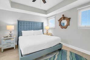 A bedroom with a bed, two bedside tables, a ceiling fan, a mirror, and a window with blinds. - Sterling Breeze 507- Dancing Waves (Panama City Beach)