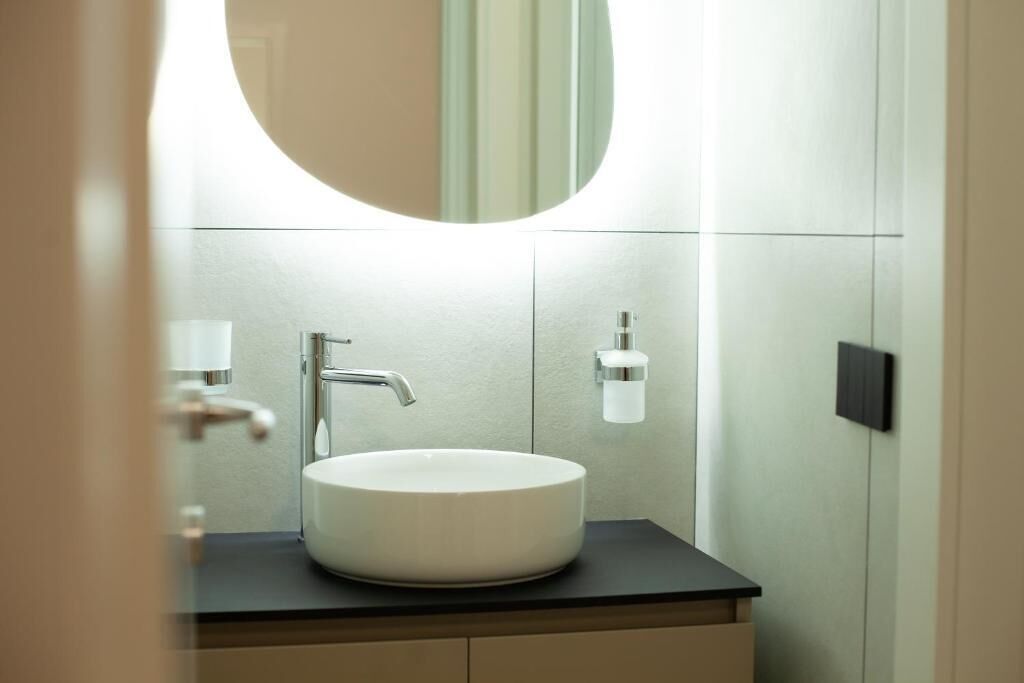 Een moderne badkamer met een rond wit wastafel, een chromen kraan en een spiegel erboven.