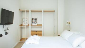 Ein Schlafzimmer mit Bett, Kleiderschrank, Wandfernseher und Nachttischlampe.
