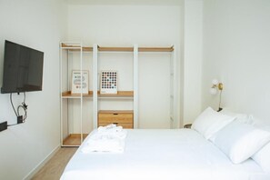 Ein Schlafzimmer mit Bett, Kleiderschrank, Wandfernseher und Nachttischlampe.