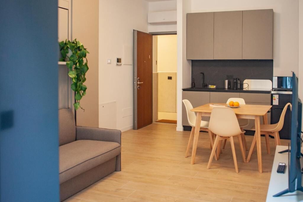 A modern living space with a sofa, dining table, chairs, and a kitchen area with cabinets and appliances.