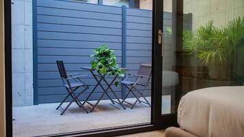 Ein Zimmer mit einer Schiebetür zum Balkon, der mit einem Tisch, Stühlen und einem Blumentopf möbliert ist. Ein blaues Geländer begrenzt den Außenbereich.