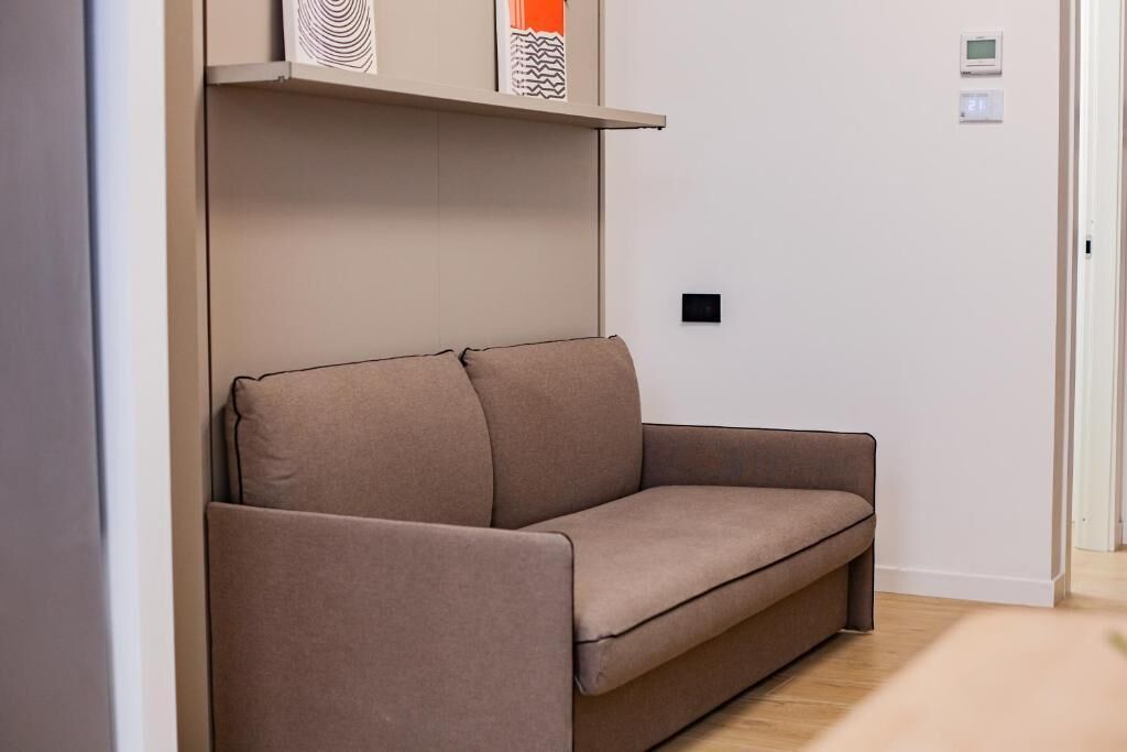 Una sala de estar moderna con un sofá, un estante con adornos y un termostato en la pared.