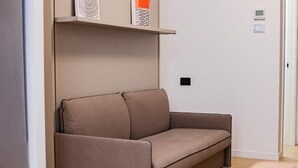 Una sala de estar moderna con un sofá, un estante con adornos y un termostato en la pared.