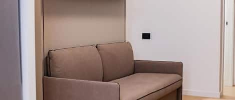 Una sala de estar moderna con un sofá, un estante con adornos y un termostato en la pared.