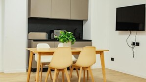 Una cocina moderna con una mesa de comedor y sillas, un televisor de pantalla plana montado en la pared y una planta en maceta sobre la mesa.