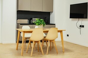 Una cocina moderna con una mesa de comedor y sillas, un televisor de pantalla plana montado en la pared y una planta en maceta sobre la mesa.