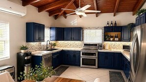 A modern kitchen with dark blue cabinets, stainless steel appliances, and a wooden ceiling.