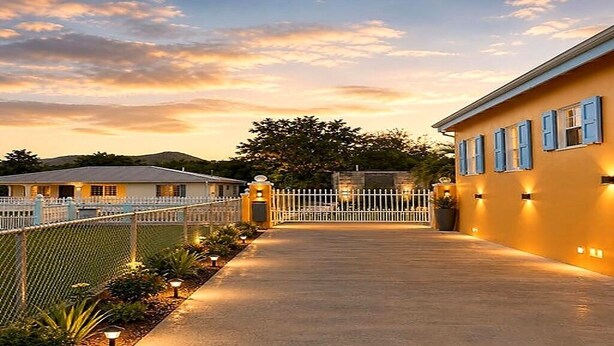 A gated property with a paved walkway leading to a building with blue shutters.