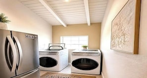 A laundry room with a stainless steel refrigerator, two front-loading washing machines, a window, and a framed artwork on the wall. - 3-bedroom house- Close Prox to Airport, Beaches and Amenities full AC (Frederiksted)