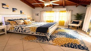A bedroom with a bed, a nightstand, a chair, a ceiling fan, and a window with curtains.
