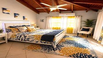 Ein Schlafzimmer mit einem Bett, einem Nachttisch, einem Sessel, einem Deckenventilator und einem Fenster mit Vorhängen.