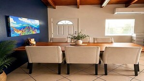 A dining area with a wooden table and chairs, a potted plant, and a painting on the wall.