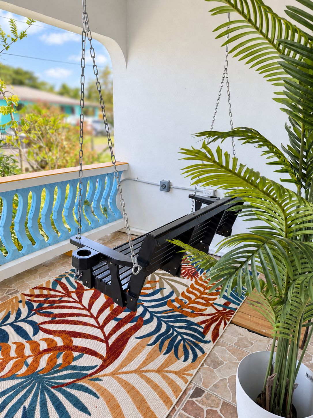Un balcon avec un fauteuil suspendu, une plante en pot et un tapis à motifs.