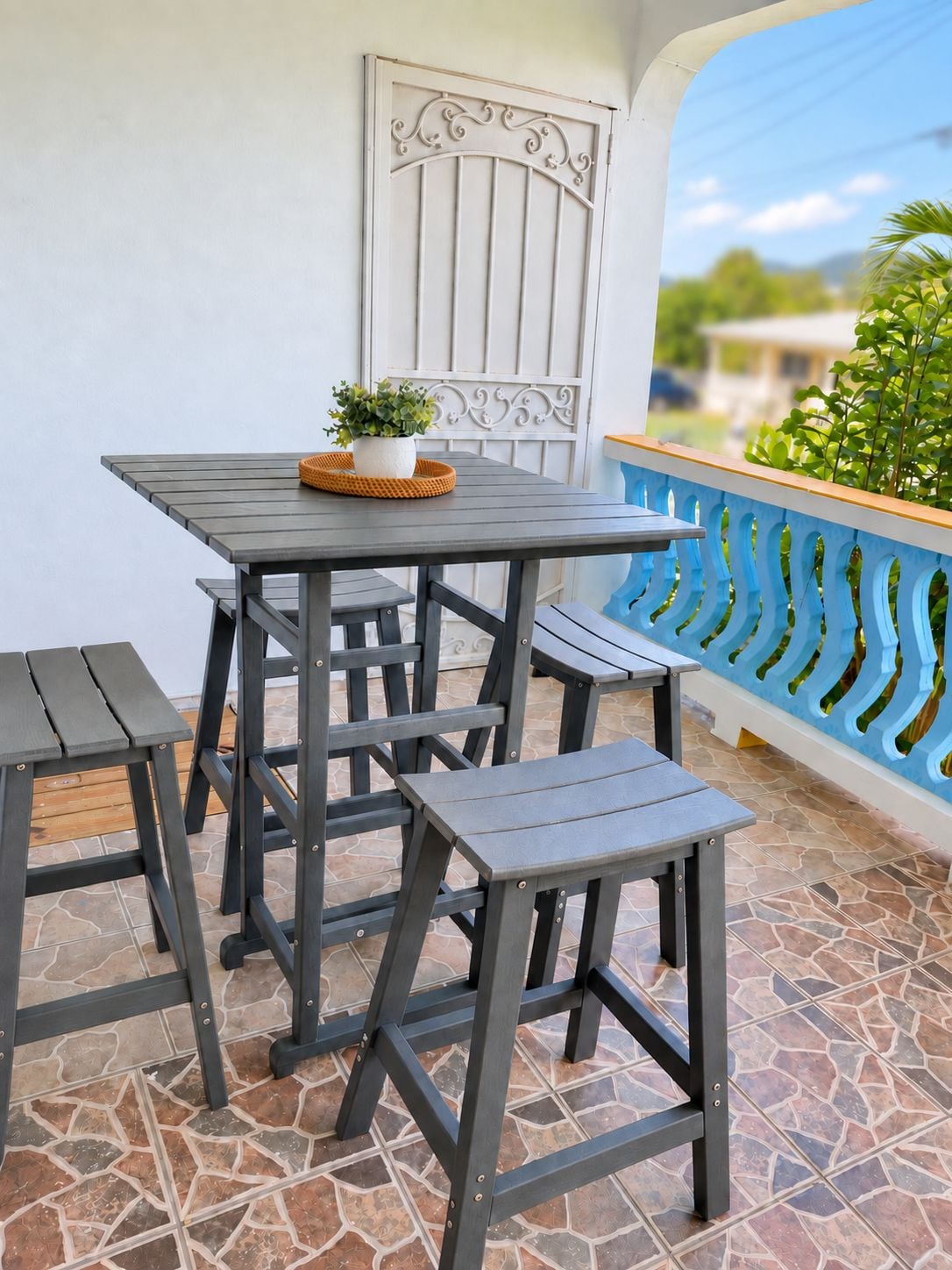 Une terrasse avec une table et deux chaises, un pot de fleurs et un portail décoratif en métal.