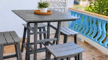 Une terrasse avec une table et deux chaises, un pot de fleurs et un portail décoratif en métal.
