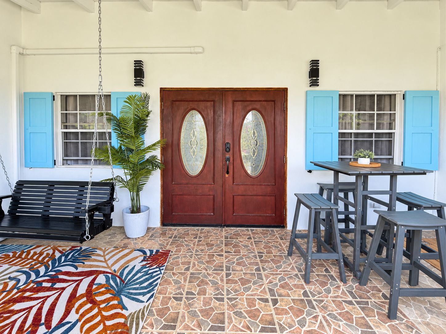 A porch with a swing, a bench, a table with stools, and a potted plant.