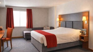 Une chambre d’hôtel avec un lit, un bureau, une chaise et une fenêtre avec des rideaux.