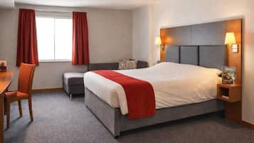 Una habitación de hotel con cama, escritorio, silla y ventana con cortinas.