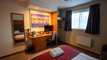A hotel room with a bed, desk, chair, and a painting on the wall.
