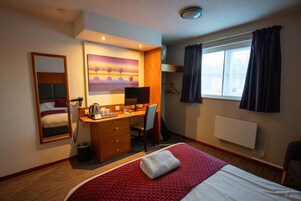 Habitación de hotel con cama, escritorio, silla y un cuadro en la pared.