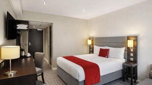 Une chambre d’hôtel comprenant un lit, des tables de chevet, un bureau, une chaise, une télévision et une porte donnant accès à une salle de bain.