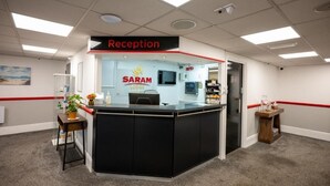 Un espace d’accueil comprenant un comptoir de réception, une enseigne indiquant « Réception » et une enseigne « SARAM LODGE ».