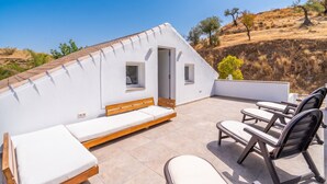 Terraço no telhado com fachada branca, um banco de madeira e várias cadeiras de descanso.