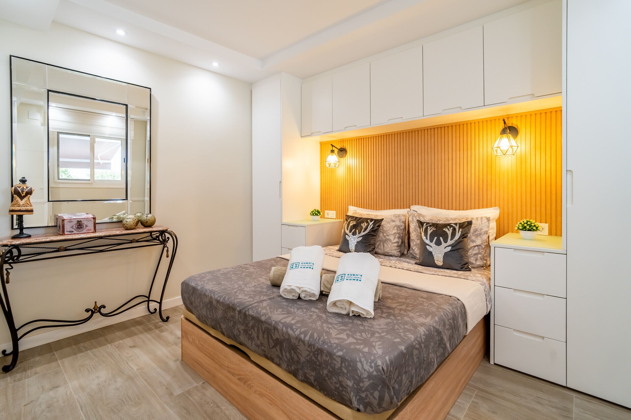 Quarto com cama, mesas de cabeceira, um espelho e parede de madeira com duas luzes de parede.