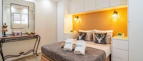 A bedroom with a bed, bedside tables, a mirror, and a wooden panel wall with two wall-mounted lights.