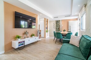 A modern living room with a flat-screen TV mounted on the wall, a wooden entertainment unit, a dining area with a table and chairs, and a green sofa. - Cubo's Violeta Rural House Family / Private pool / BBQ / Air conditioning / Free Wi-Fi (Coín)