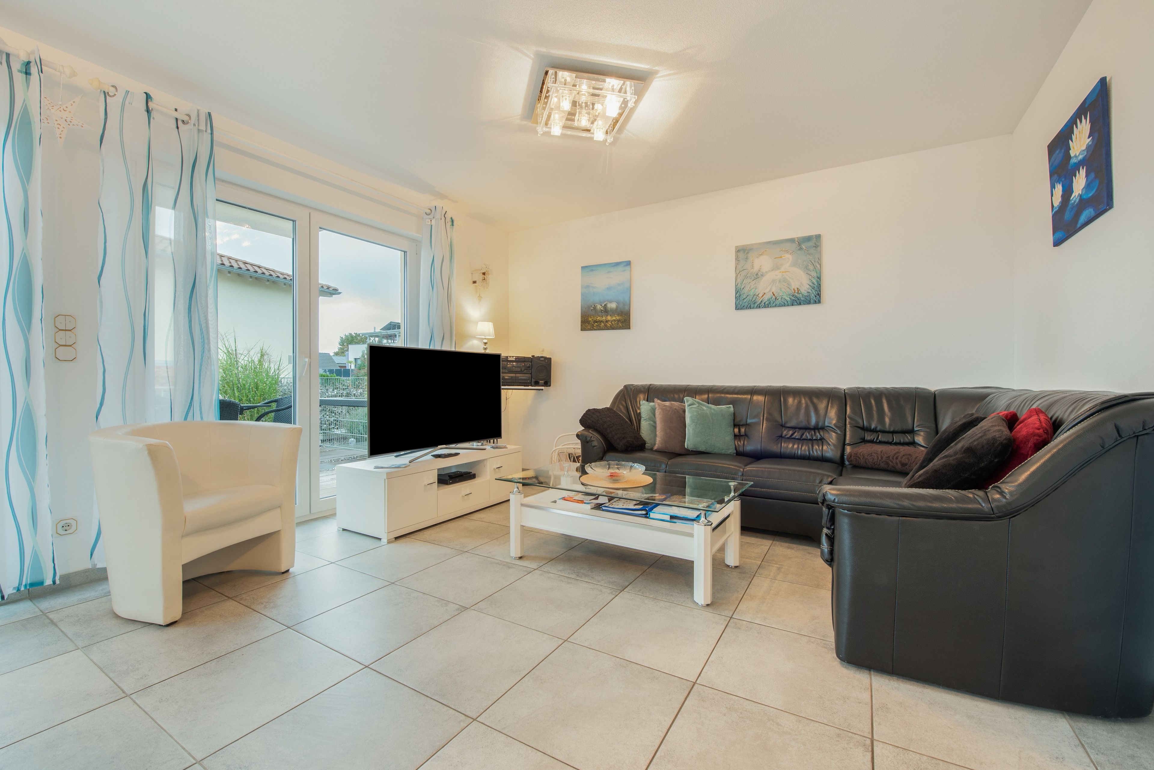 A living room with a flat-screen TV, a sofa, a coffee table, and a balcony with a view.