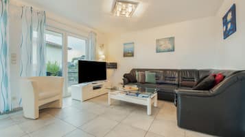 A living room with a flat-screen TV, a sofa, a coffee table, and a balcony with a view.