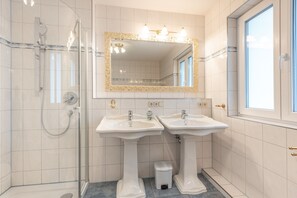 A bathroom with two sinks, a shower, and a mirror with ornate gold detailing.