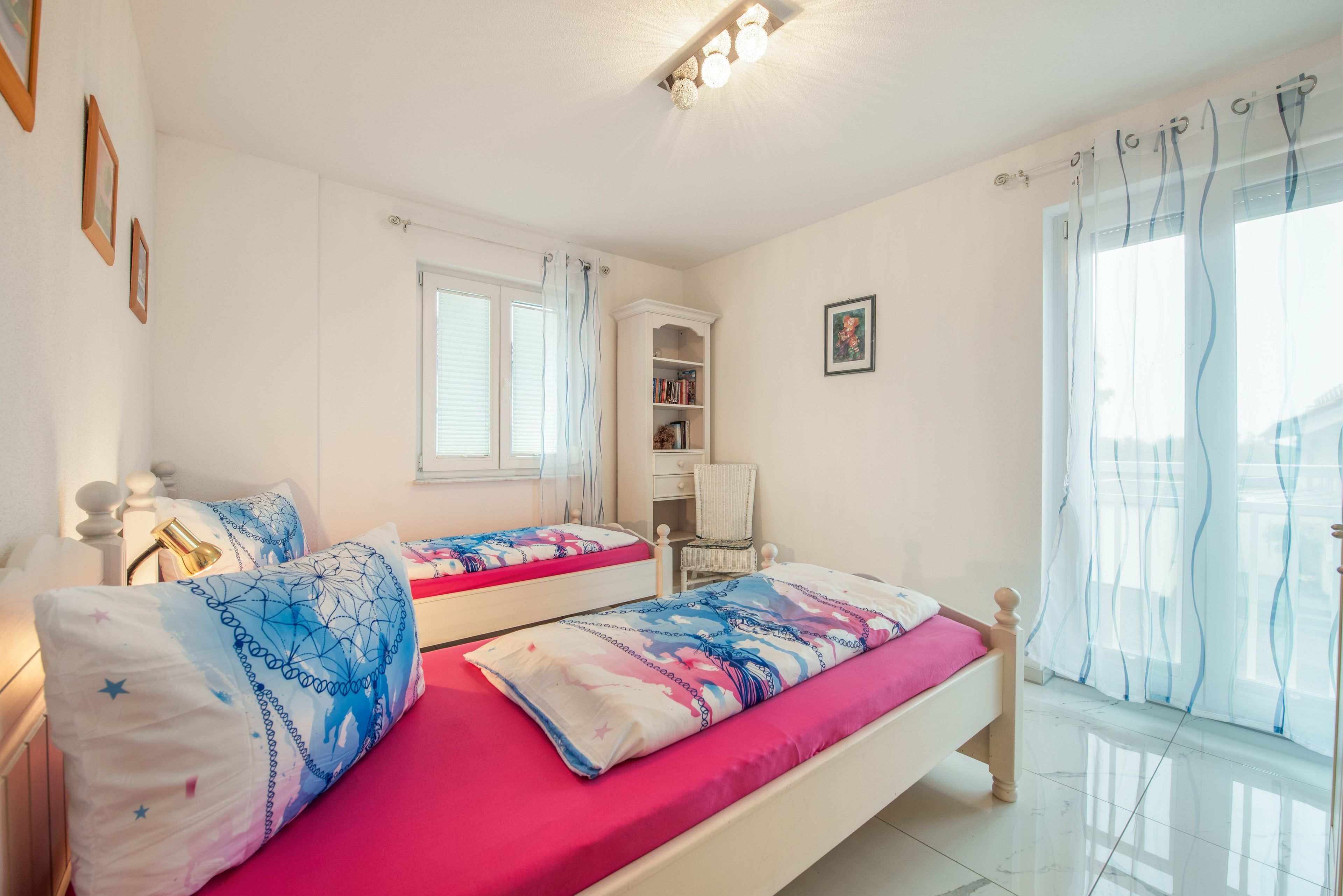 Un dormitorio con dos camas, una ventana, una estantería y una silla.