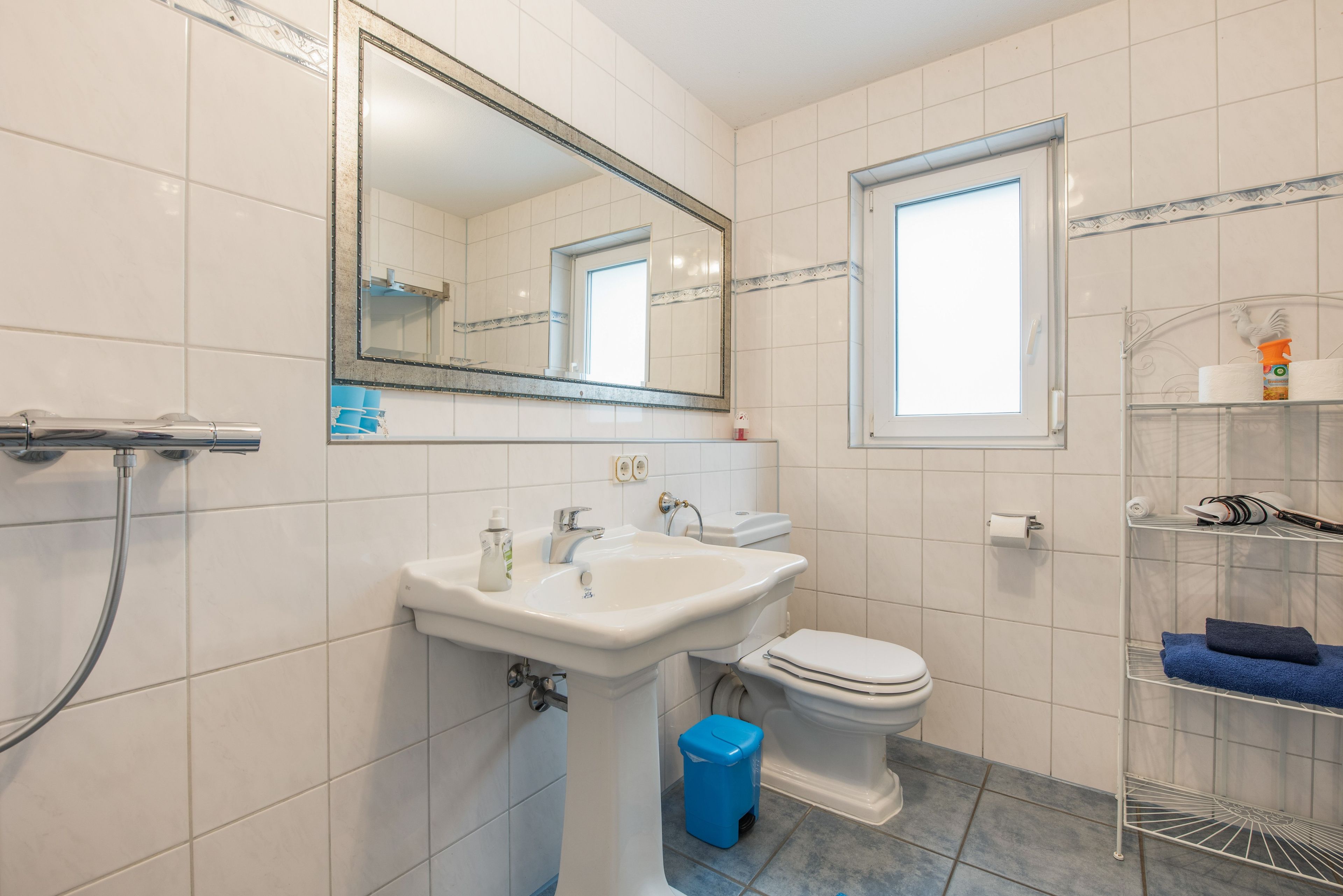 Ein Badezimmer mit einem weißen Waschbecken, einer Toilette, einem Spiegel und einem Fenster.
