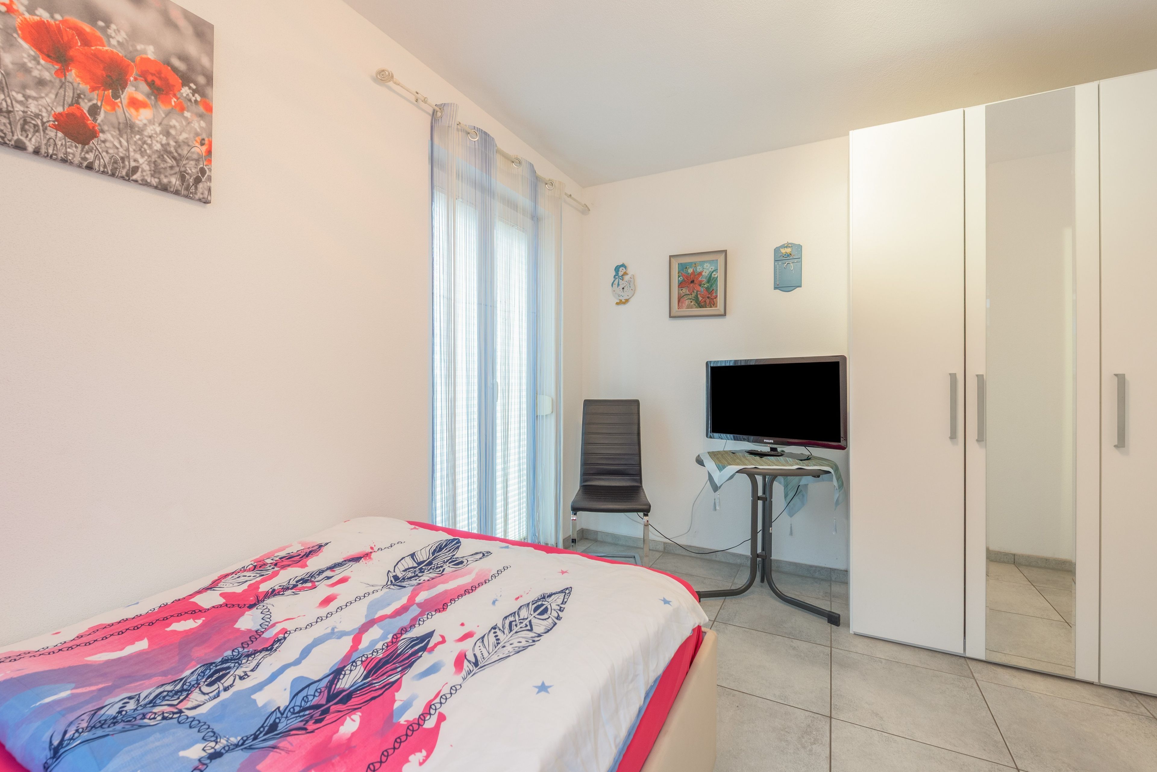 Ein Hotelzimmer mit Bett, Fernseher, Schreibtisch und Kleiderschrank.