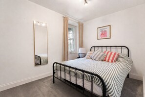 A bedroom with a bed, a mirror, a window with curtains, a bedside lamp, and a framed picture on the wall. - Central Edinburgh Retreat with Sunny Garden (Edinburgh)
