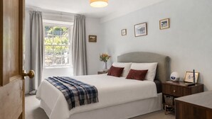 Un dormitorio con cama, mesita de noche, lámpara y ventana con cortinas.