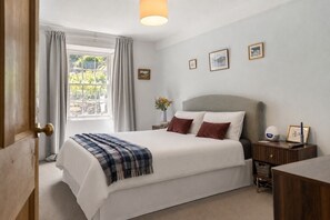 Ein Schlafzimmer mit Bett, Nachttisch, Lampe und einem Fenster mit Vorhängen.