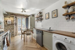 A kitchen with a stone wall, wooden flooring, a dishwasher, a washing machine, and a dining area with chairs and a table. - Central Edinburgh Retreat with Sunny Garden (Edinburgh)
