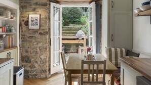 Una cocina rústica con pared de piedra, mesa de madera y puerta abierta a un jardín.