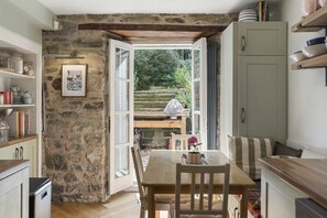 Eine rustikale Küche mit Steinwand, Holztisch und offener Tür zu einem Garten.
