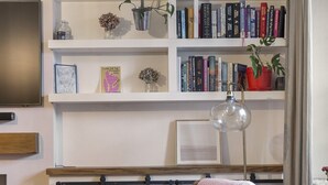 Una sala de estar acogedora con un sillón de madera, una estantería llena de libros, un televisor de pantalla plana y una planta pequeña.